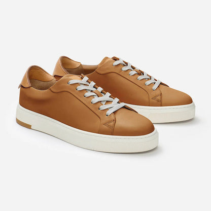 Pair of tan sneakers with white laces on a light gray background